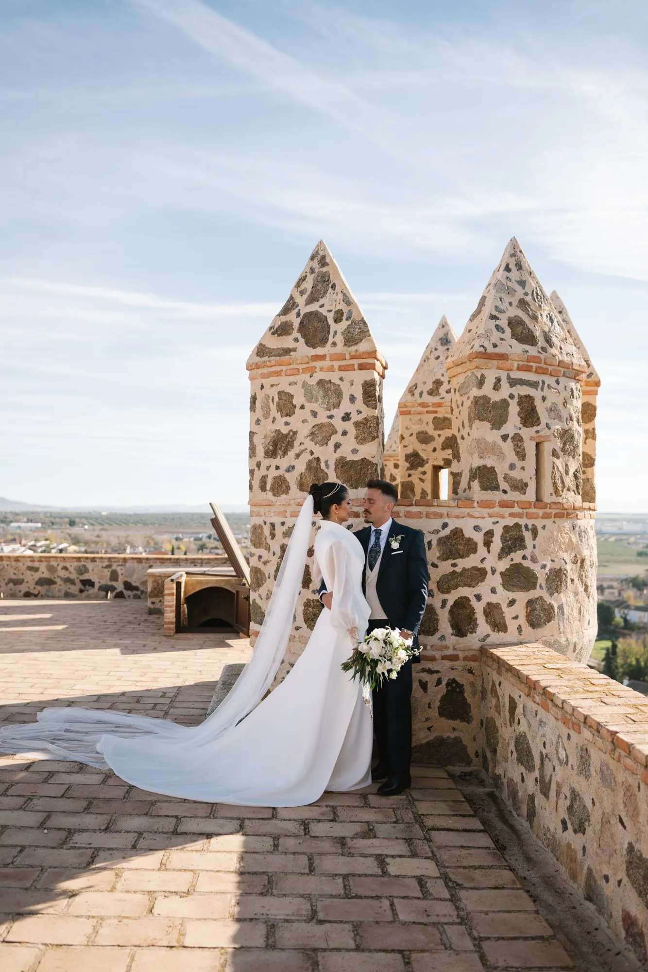 Antonio and Ainara between the towers of Castillo de Guadamur, with the Toledo plain behind them