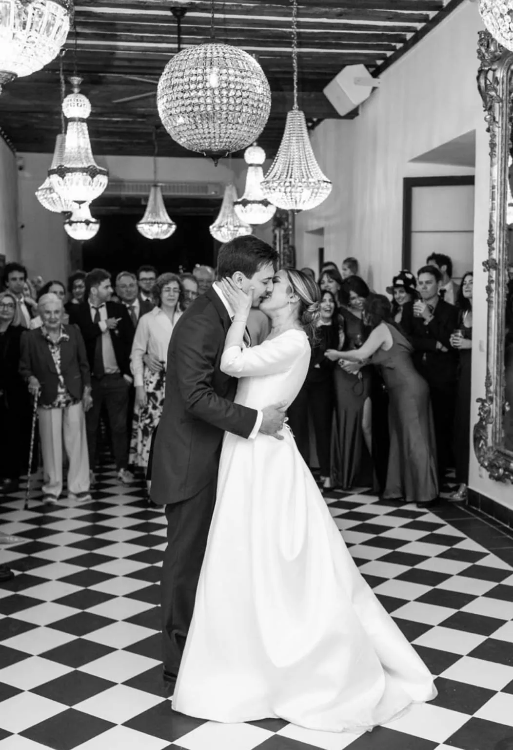 Los novios besándose en el baile, bajo lámparas de araña y sobre un suelo de ajedrez, en blanco y negro