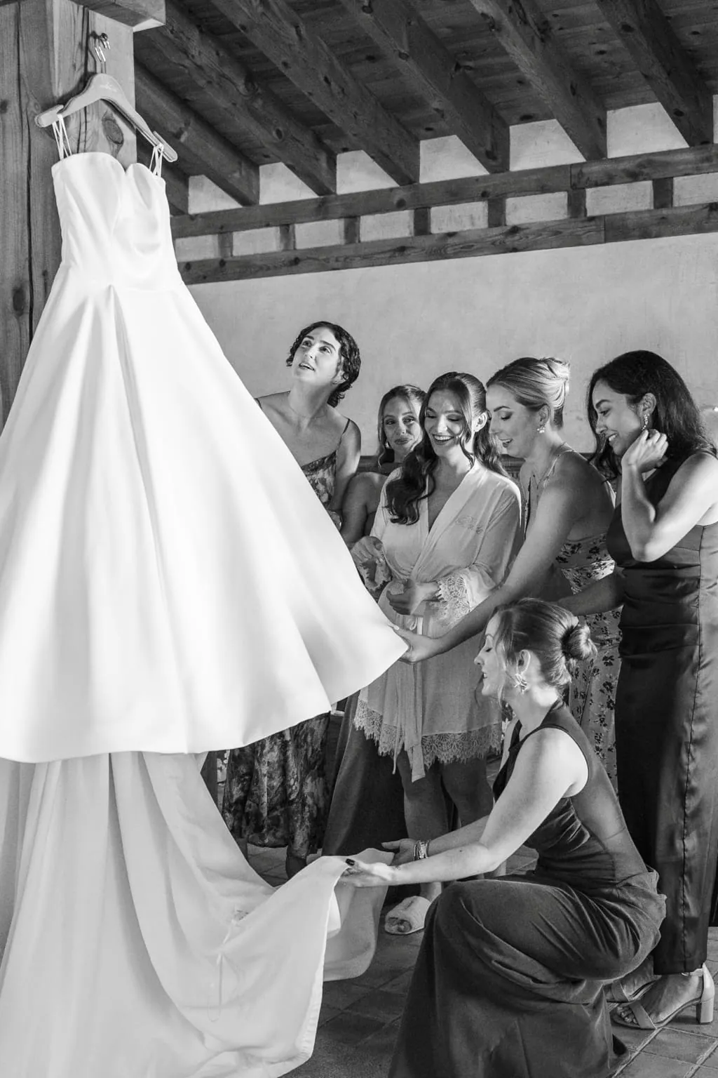 El vestido de novia colgado y las damas de honor mirándolo, en blanco y negro