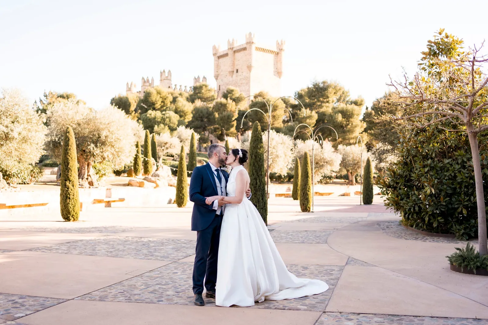 Jessica and Raúl in a garden of cypress trees, with the castle in the background