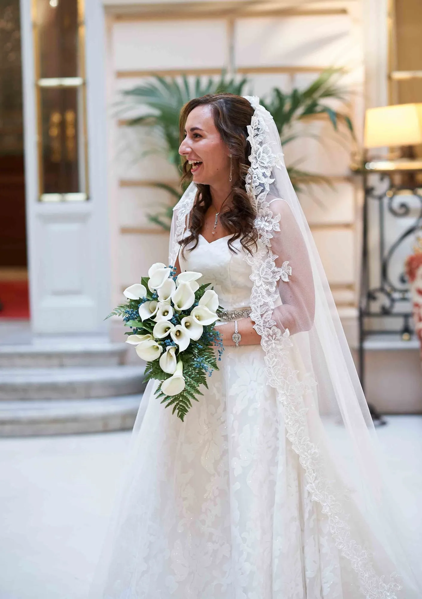 Bride in a lace mantilla with a bouquet of white calla lilies, laughing on her wedding day