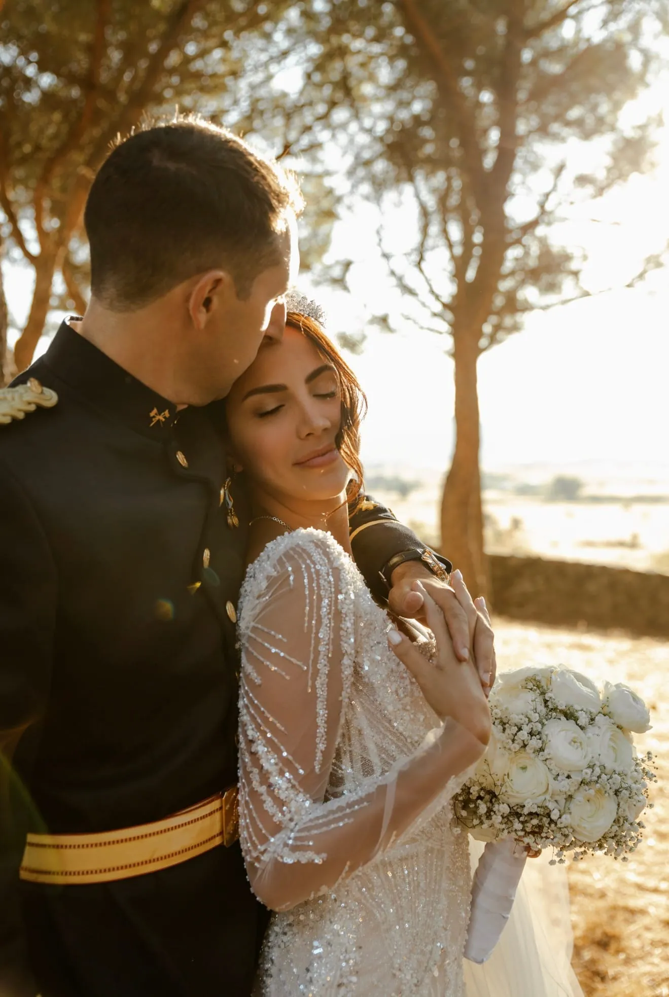 Groom in full dress uniform embracing the bride at sunset