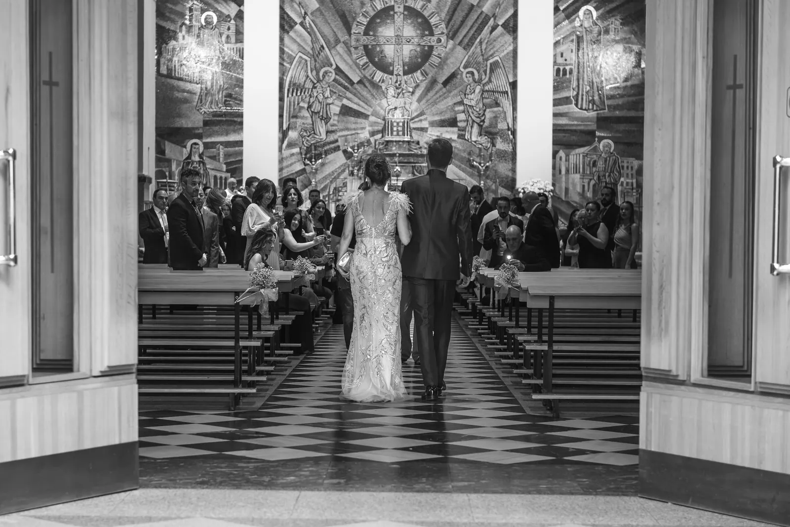 A couple at the end of a church aisle, in black and white